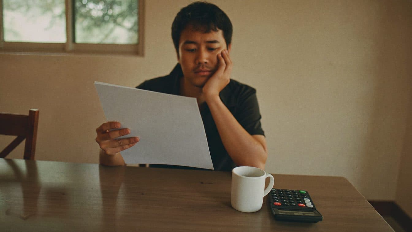 A worried man reviewing a printed tax bill at his kitchen table at home